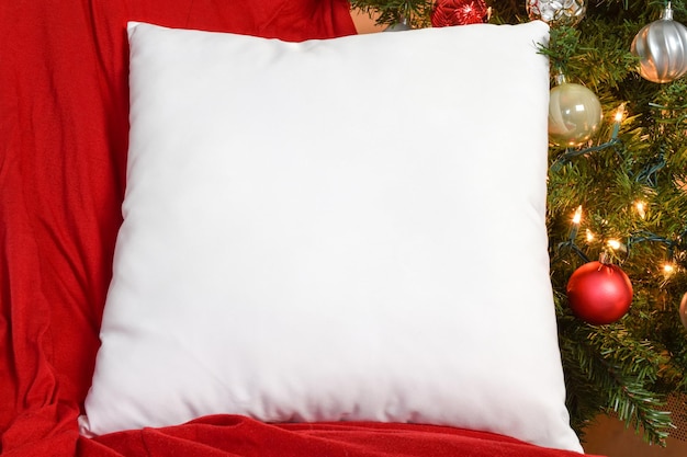 white square pillow mockup resting on red blanket with lit up christmas tree in background