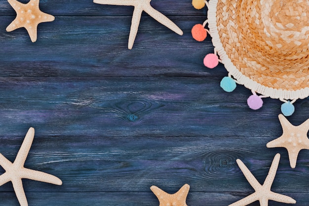 White starfish and a small straw hat with colored pompons on a blue wooden background copy space.