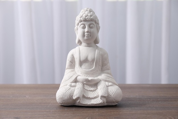 White statue of Buddha on wooden table on light background