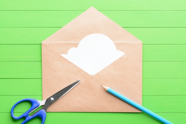 White sticker in the shape of clouds in the envelope on green wooden background