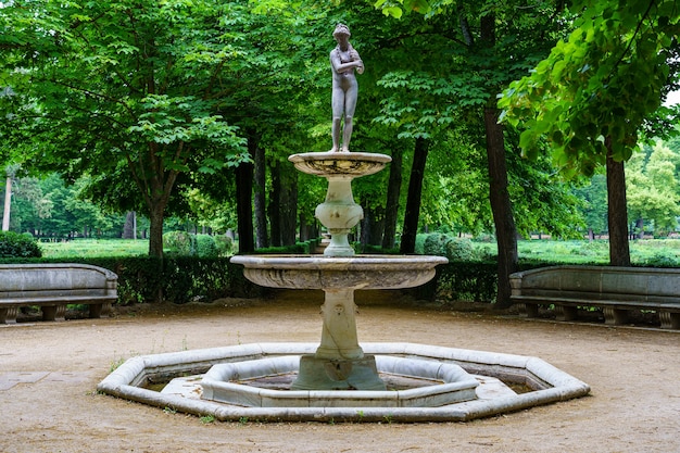 White stone fountain with statue in public park with green vegetation