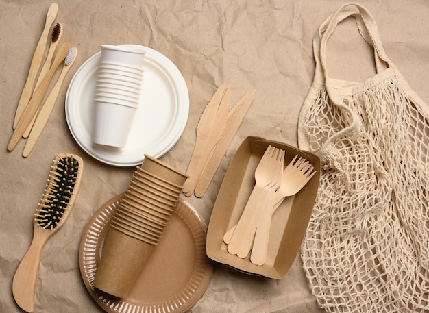 White string bag with disposable paper dishes and wooden forks on brown kraft paper, top view