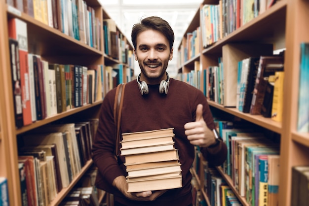 White student in sweater with books in aisle of library.