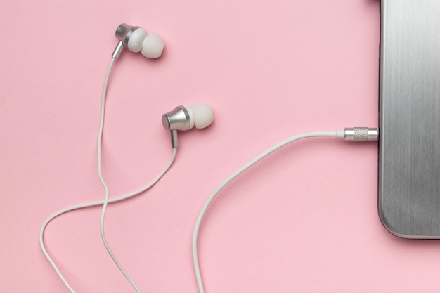 White stylish headphones connected to a laptop on a pink background The concept of business and education