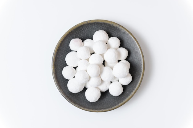 Белые сахарные шарики в серой керамической тарелке на белом фоне. Крупный план, вид сверху.