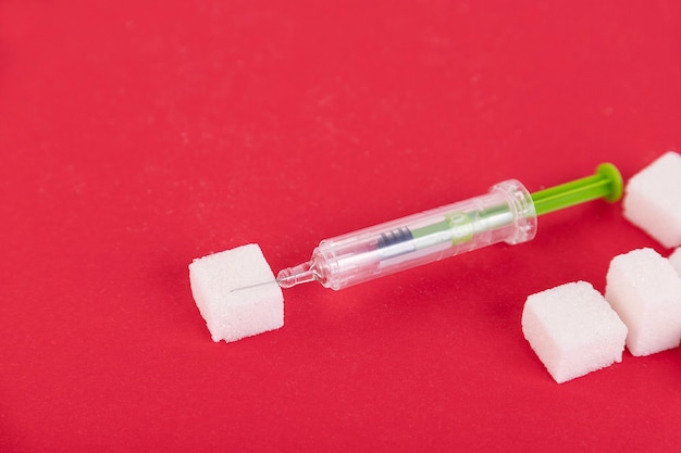 Photo white sugar cubes and insulin syringe on a red background. copy space.