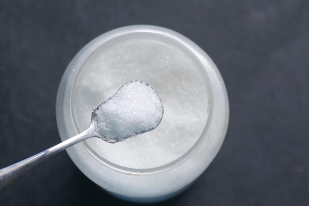 White sugar and spoon in a container on black background