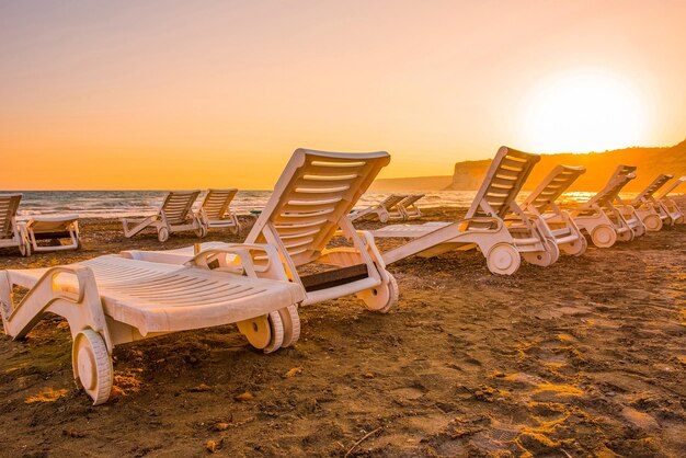 White sunbeds in a sandy beach at sunset