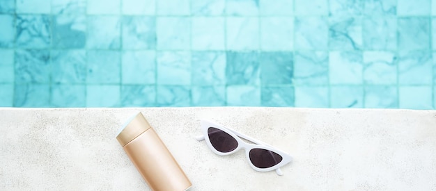 Белые солнцезащитные очки бутылка солнцезащитного крема и шляпа возле бассейна в роскошном отеле Концепция летних путешествий, каникул и выходных