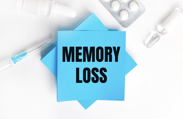 Su una superficie bianca, una siringa, una fiala, pillole, una fiala di medicinale e adesivi azzurri con la scritta memory loss