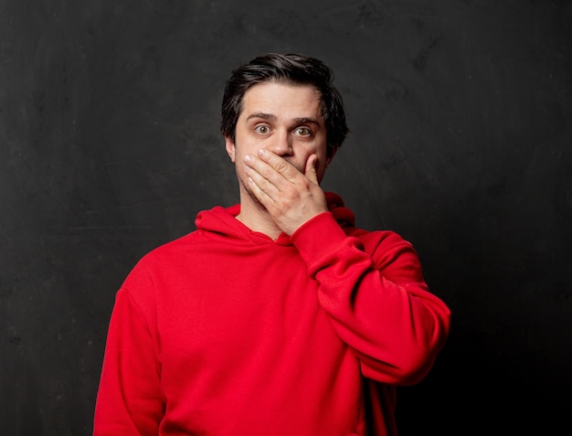 White surprised guy in red sweatshirt on dark wall