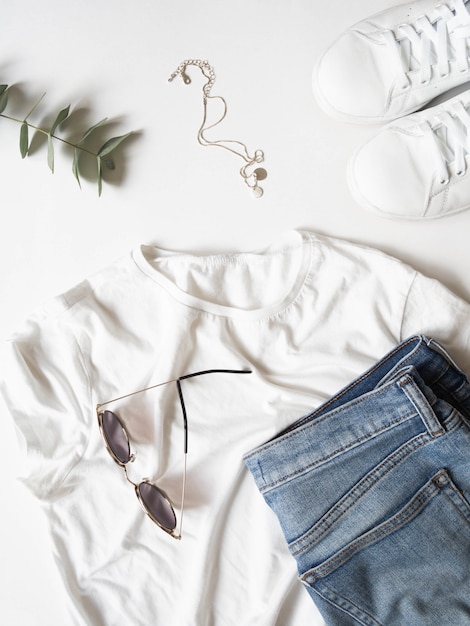 White t-shirt blue jeans, sunglasses, necklace and white sneakers on white background.