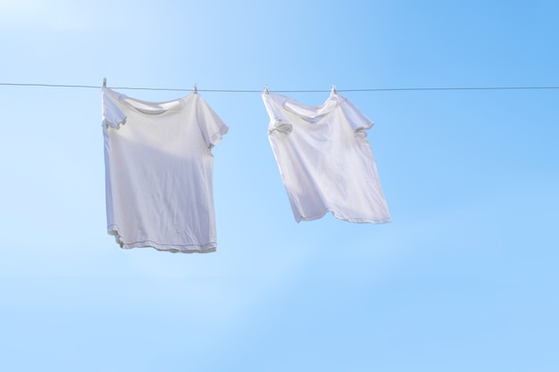 Белая футболка на бельевой веревке против голубого неба