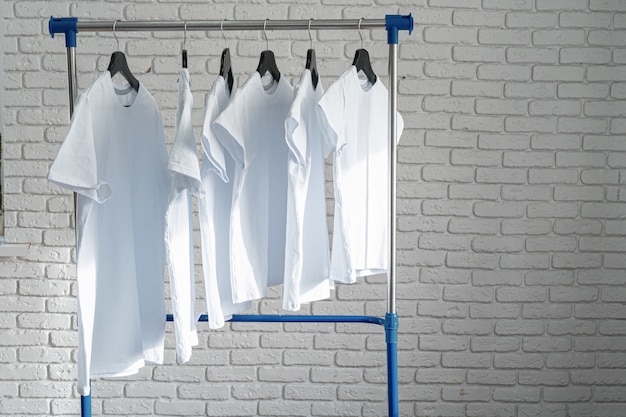 White t-shirt hanging on hanger against brick wall, copy space