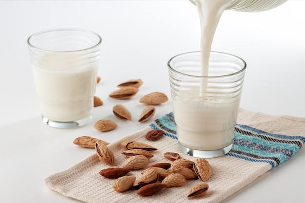 On a white table almond milk in a glass with almonds