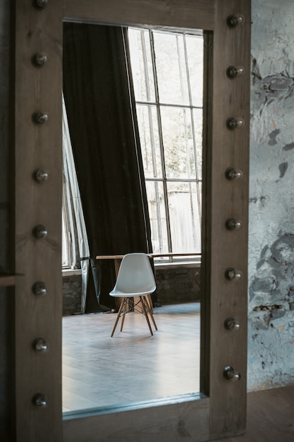 Photo white table or armchair is reflected in large floor mirror in studio.