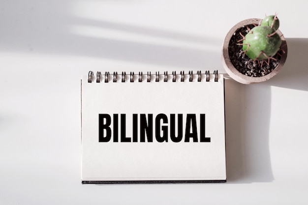 白いテーブルの上に花、BILINGUALという言葉が書かれたノート