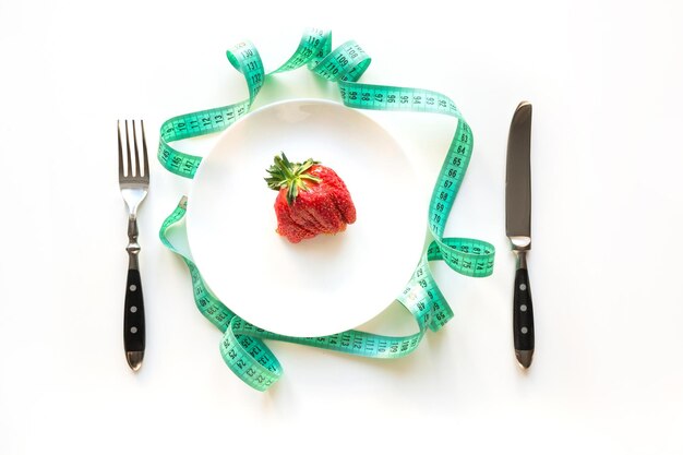 White table setting with tape measure and one ugly organic strawberry Concept weight loss for Detox