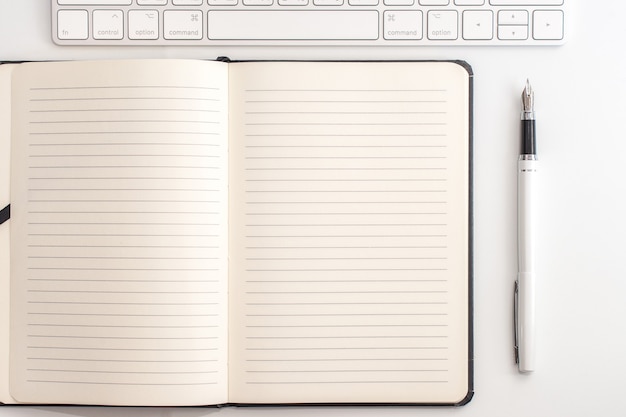 White table with notepad, keyboard and fountain pen. View from above