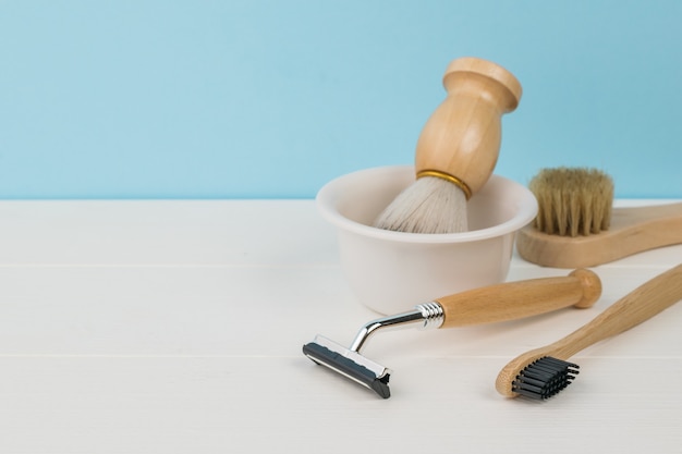 A white table with shaving accessories on a blue background. Space for the text.