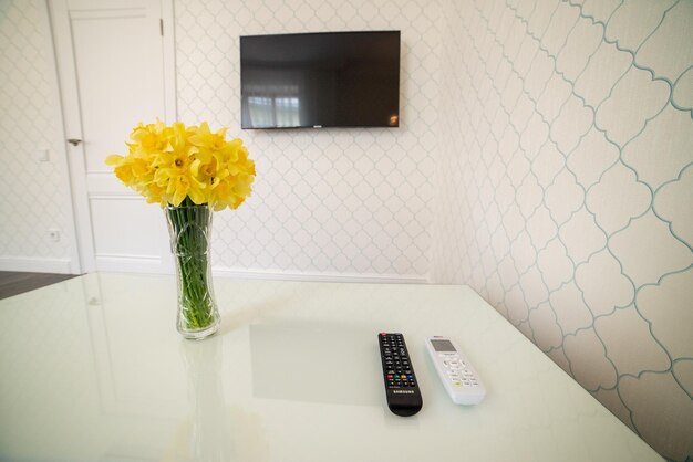 Photo a white table with a tv and a remote next to a vase with flowers.