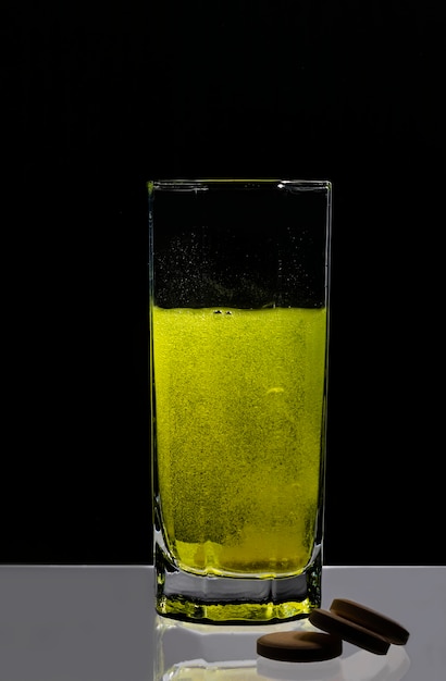 Una compressa bianca si dissolve in un bicchiere d'acqua e trasforma l'acqua in giallo su sfondo nero