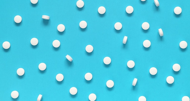 White tablet pills on a blue background top view medical background backdrop