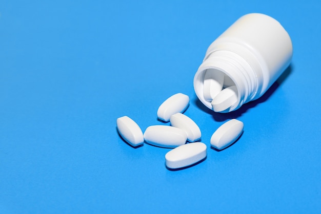 White tablets scattered from a plastic bottle on a blue background. Top view with copy space.