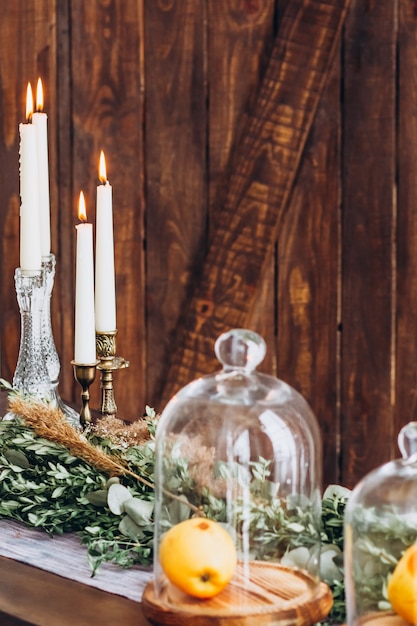 White tall candles in crystal candlesticks, candles on aged rustic wooden textured background.