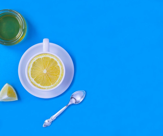 Photo white tea cup with fresh halved lemon and honey on the blue background copy space top view