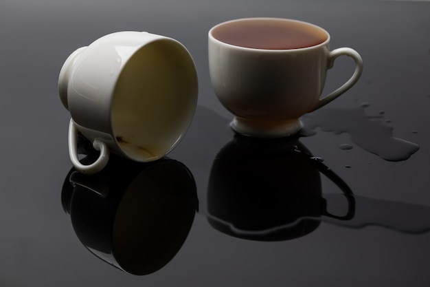 Белая чашка чая с полным стаканом воды, помещенная на черном фоне с отражением.