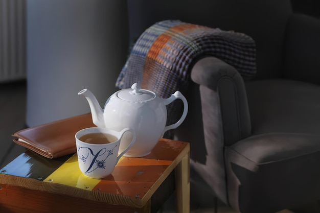 White teapot and cup with tea in home interior