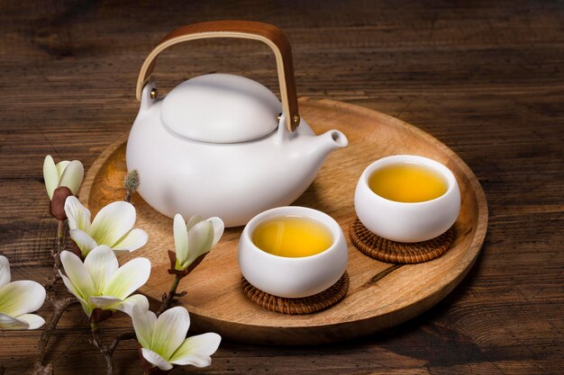 A white teapot and two cups of lemongrass tea on a wooden tray View from above