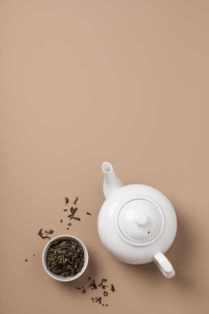 White teapot with a bowl of green tea on a beige background top view