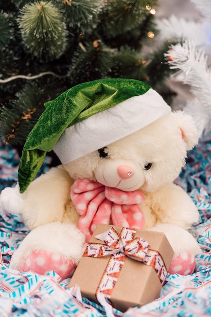 White teddy bear sits with a gift near the christmas tree