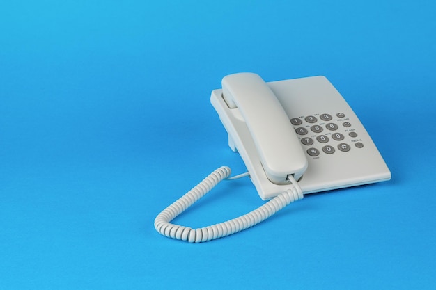 A white telephone with gray buttons on a blue background. The concept of telephone communication.