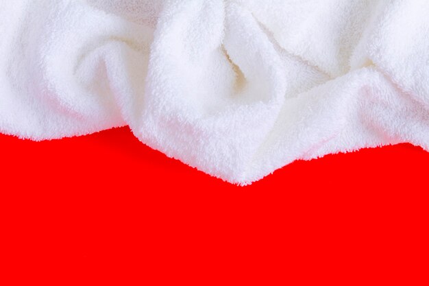 Белое махровое полотенце на красном фоне. Вид сверху. Скопируйте пространство. Крупный план.
