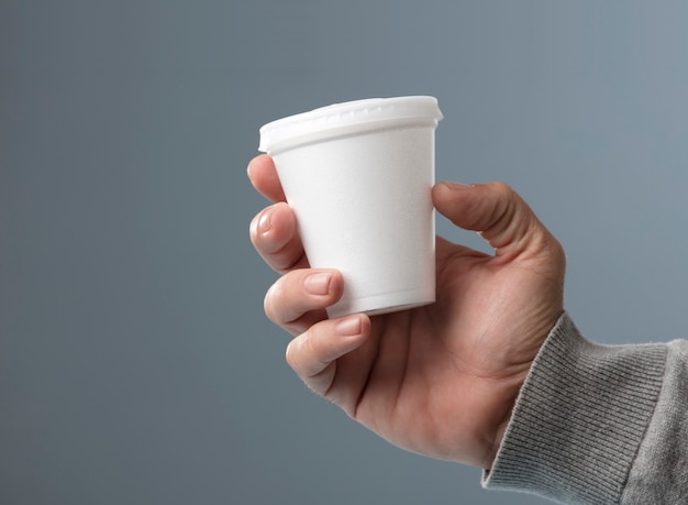 white thermal glass with lid in hand gray background