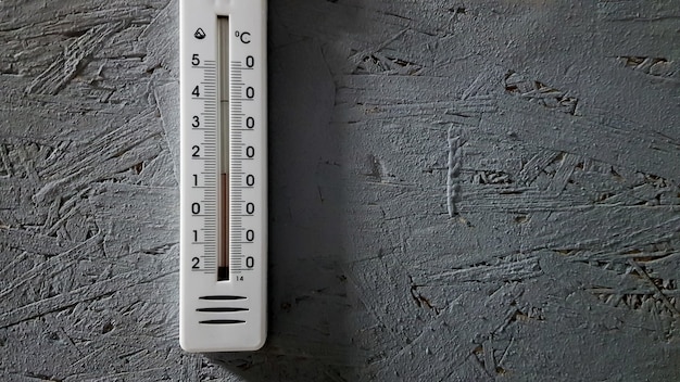 White thermometer hanging on a gray gray wooden wall indoors, background with copy space and empty place for your text.