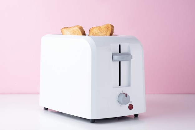 White toaster with  roasted toast bread on pink background, close up