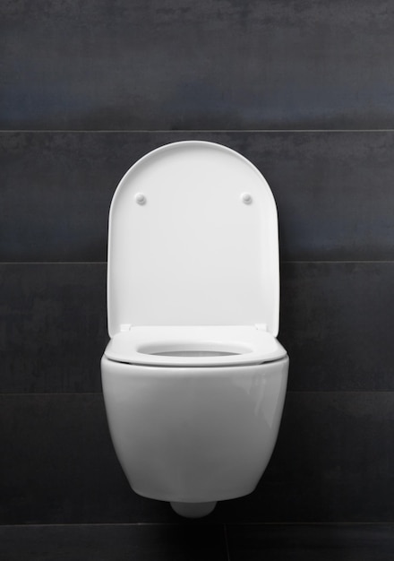 White toilet bowl on a black wall in a bathroom interior