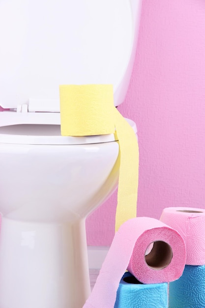 Photo white toilet bowl and colorful rolls of toilet paper in bathroom