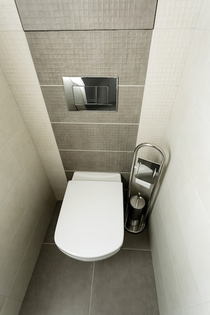 White toilet bowl in modern bathroom with paper holder and toilet brush.