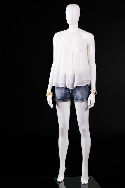 Фото Белый топ и джинсовые шорты. женский манекен в белом топе. летний наряд на темном фоне. стильный образ барышни.