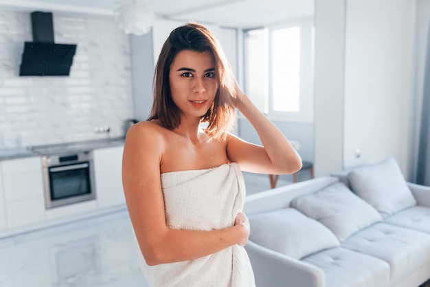 In white towel Young woman is indoors in room of modern house at daytime