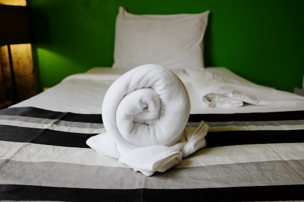 Белые полотенца свертываются на кровати в спальне отеля