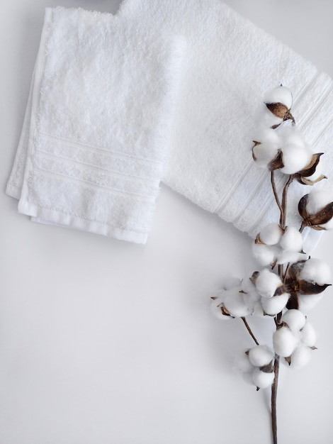 Foto asciugamani bianchi con ramo di fiori di cotone su fondo bianco