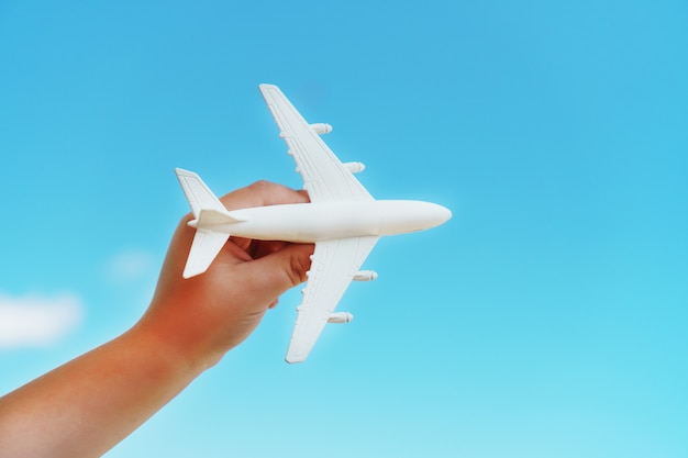 青い空を背景に子供の手に白いおもちゃの飛行機
