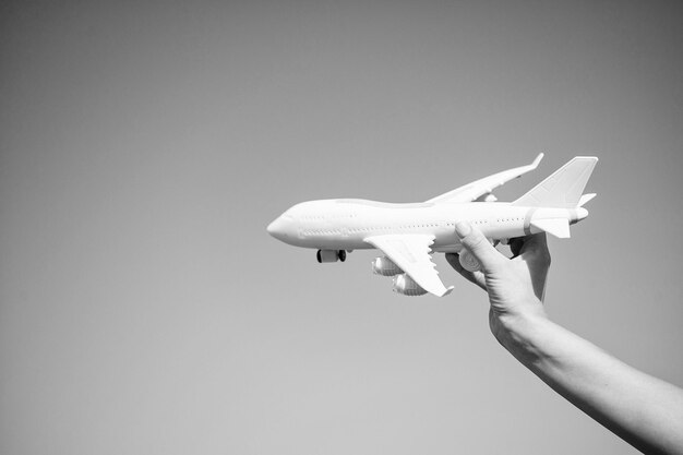 日当たりの良い青い空の背景に女性の手で白いおもちゃの飛行機ビジネス旅行と休暇の自由とインスピレーション航空便と郵便配達のコンセプトコピースペース