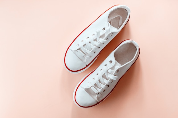 White trendy white sneakers on creamy peach background. Flat lay, top view. Place for text. Minimalistic style composition.